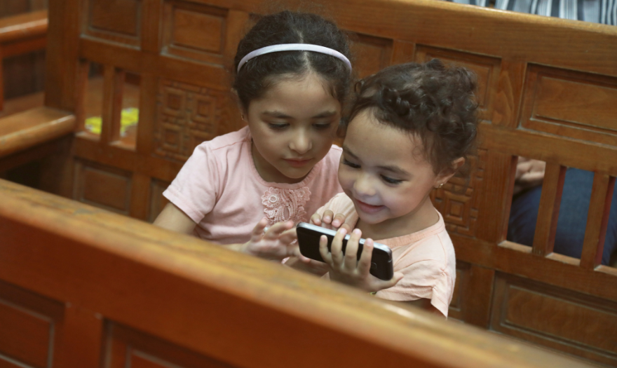 Egyptiläiset lapset tutkivat kännykkää kirkonpenkissä