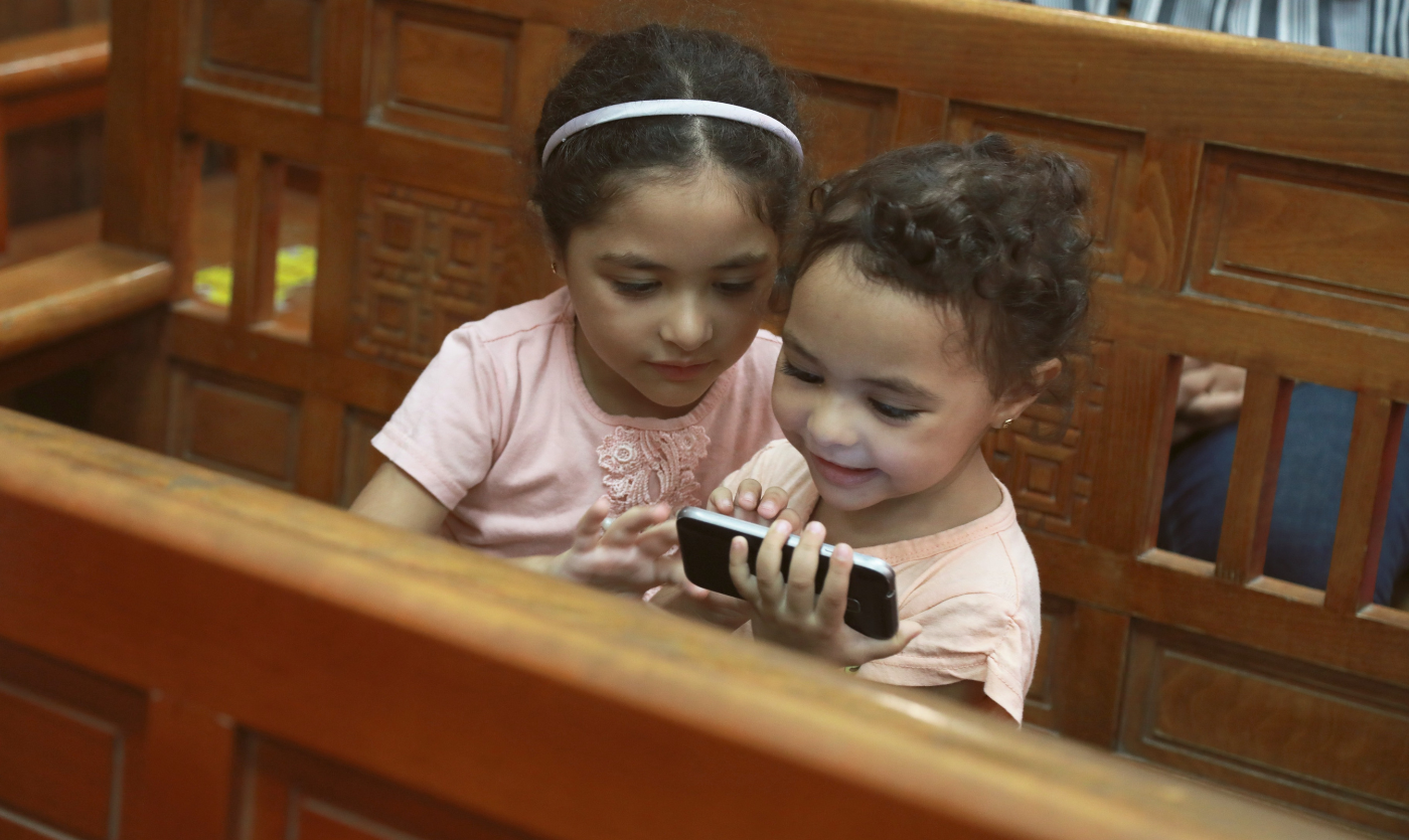 Egyptiläiset lapset tutkivat kännykkää kirkonpenkissä