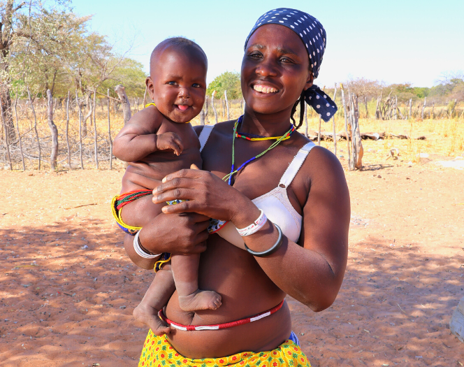 nainen perinteisessä dhimba vaatteessa hymyilee vauva sylissään