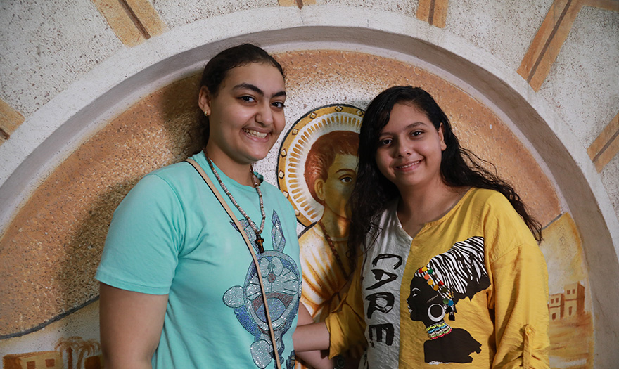 Kaksi nuorta egyptiläistä naistaposeeraa ikonikuvan edessä.