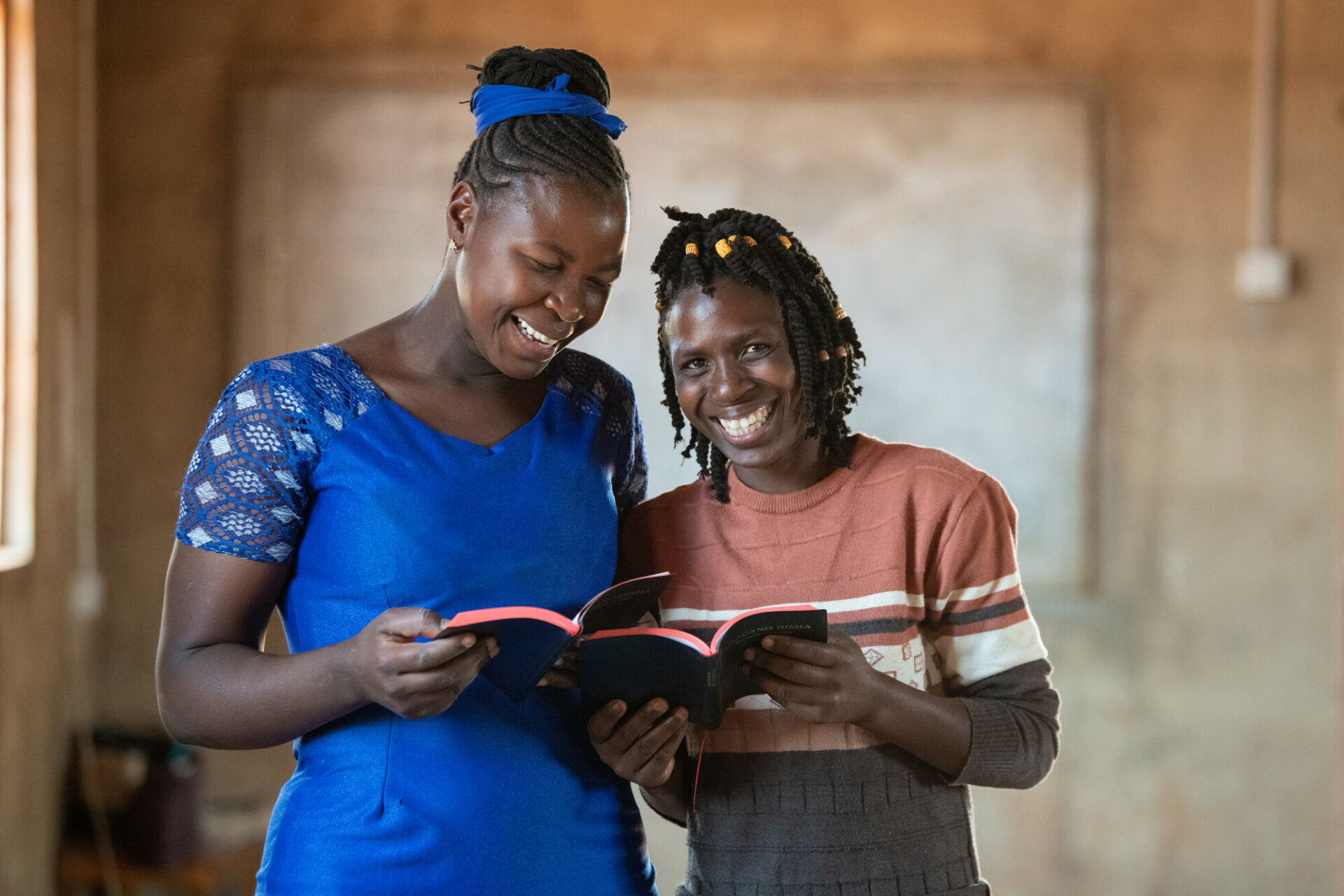 kaksi naista Raamatut käsissään hymyilevät kameralle