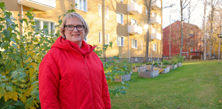 Nainen punaisessa takissa hymyilee ja katsoo kameraan