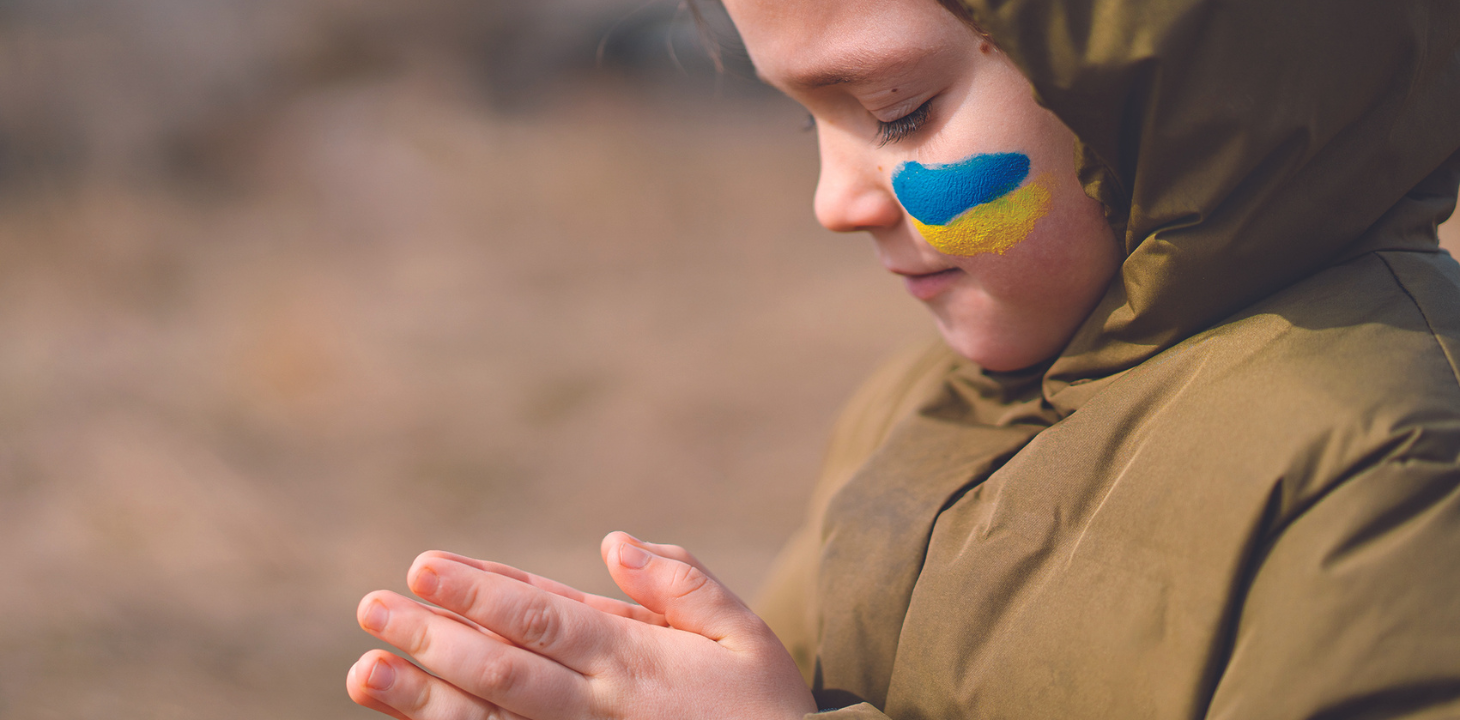 tyttö rukoilee, poskessa ukrainan lippu