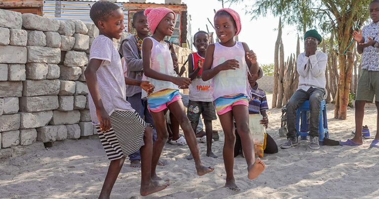 Namibialaiset lapset tanssivat ulkona iloisesti hymyillen.