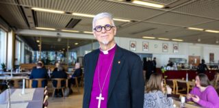 Piispa violetissa paidassaan katsoo suoraan kameraan