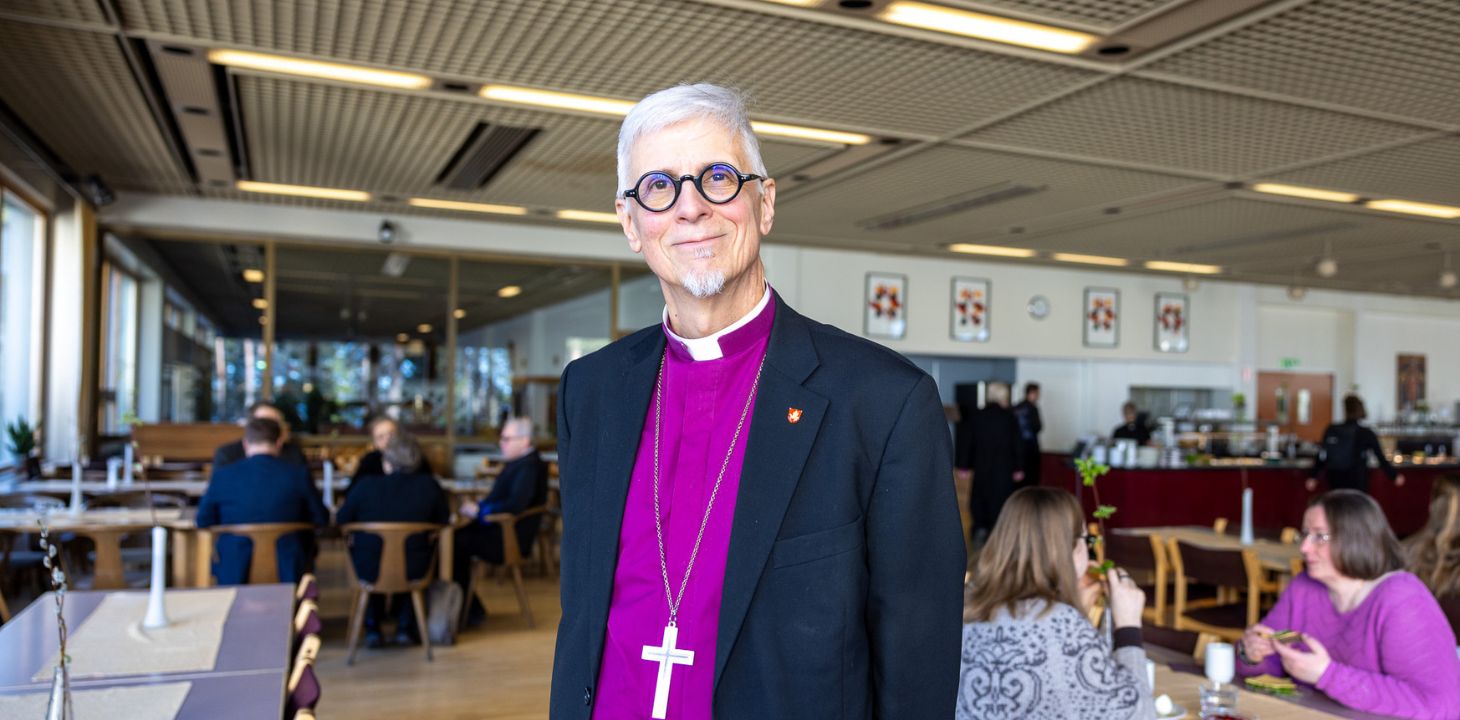 Piispa violetissa paidassaan katsoo suoraan kameraan