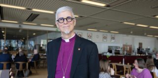 Mies piispan paidassa kahvilassa katsoo suoraan kameraan