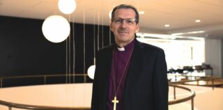 Mies piispan paidassa sisätiloissa risti kaulassaan