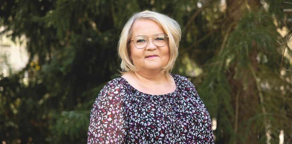 Nainen ulkona katsoo suoraan kameraan ja hymyilee