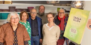 kuusi ihmistä seisoo Piplian raamattukaupassa, päällä iso kuva Tässä olen kirjasta