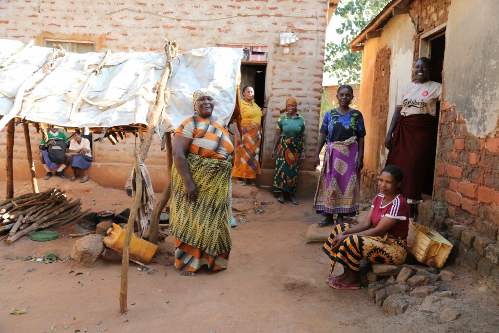 Tansanialaisen Maguhan kylän naisia kotiensa edessä. Taustalla naisten yhteinen ulkokeittiö.