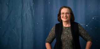 Nainen sinisellä taustalla katsoo suoraan kameraan