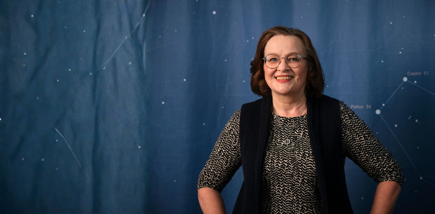 Nainen sinisellä taustalla katsoo suoraan kameraan