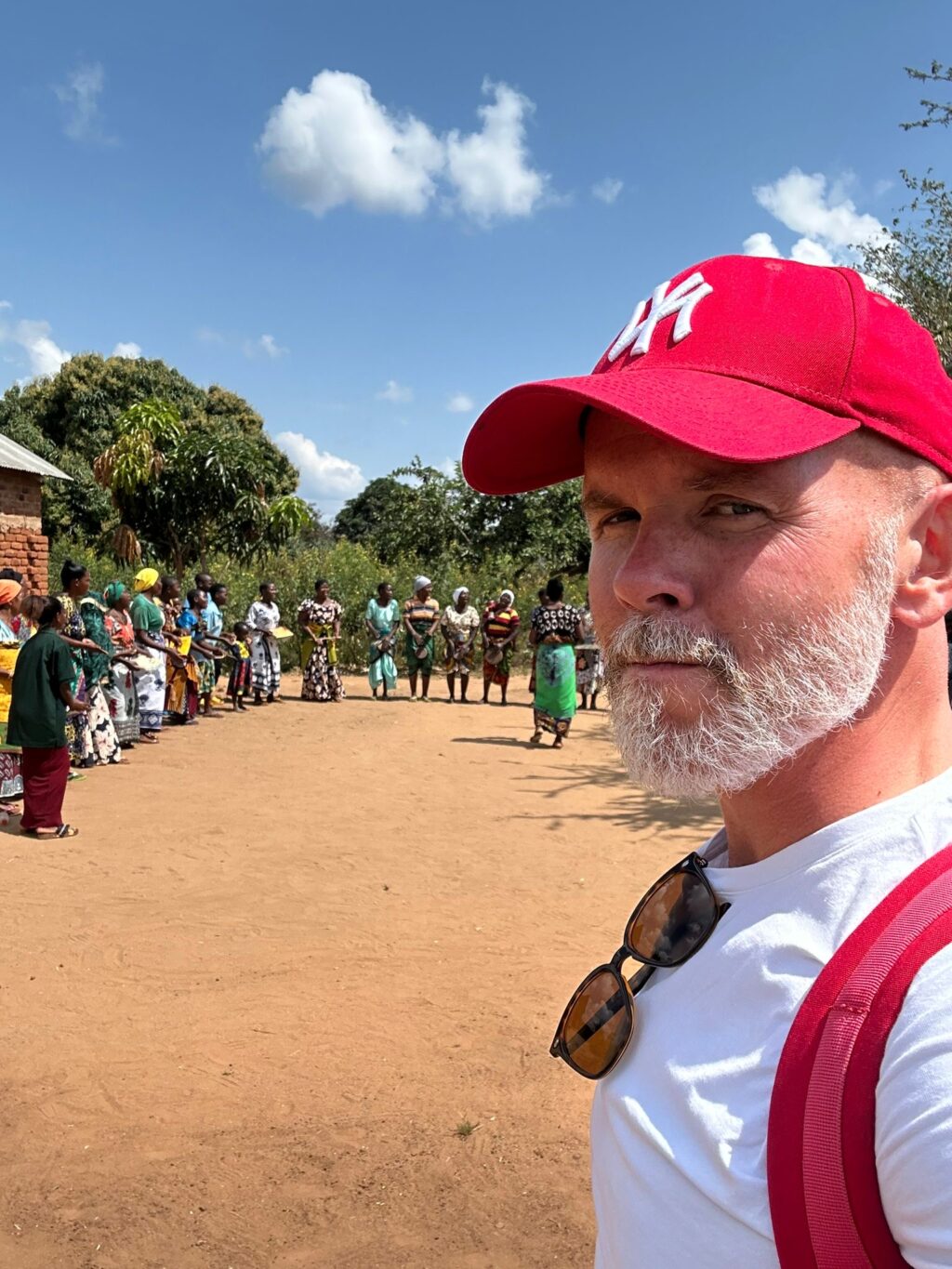 Piplian varainhankinnan suunnittelija Mikko Huttunen Tansaniassa. Taustalla näkyy naisten lukutaitoluokkien oppilaita värikkäissä vaateissa rivissä ja sinistä Tansanian taivasta.