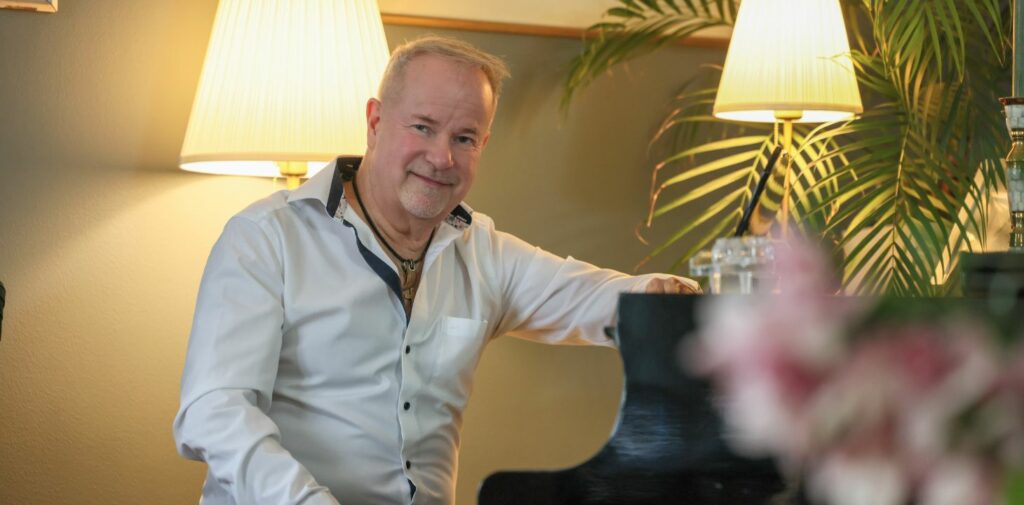 mies kauluspaidassa istuu flyygelin äärellä