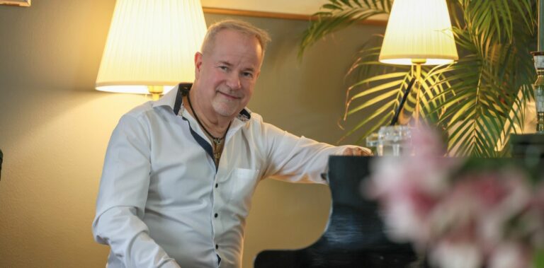 mies kauluspaidassa istuu flyygelin äärellä