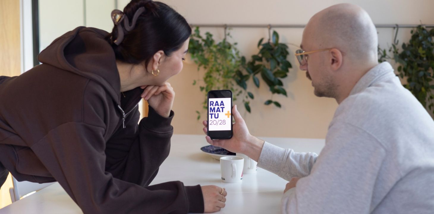 nainen ja mies pöydän ääressä, katsovat puhelimesta Raamattu 2028